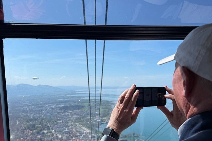 A person taking a photo with a smartphone, overlooking a landscape with mountains and a body of water. 4