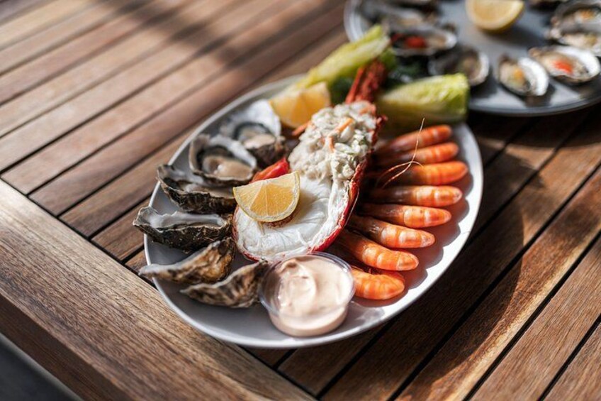 Une table en bois sur laquelle est disposé un plateau de fruits de mer comprenant des huîtres, des crevettes et des tranches de citron. 5