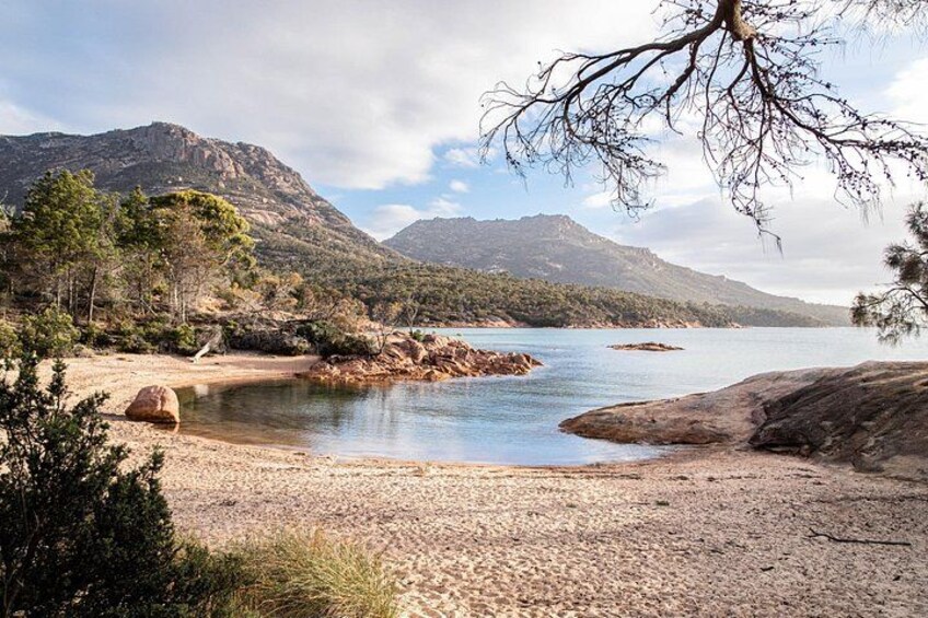 Un paisaje costero con playa, costa rocosa, agua tranquila y montañas al fondo. 4