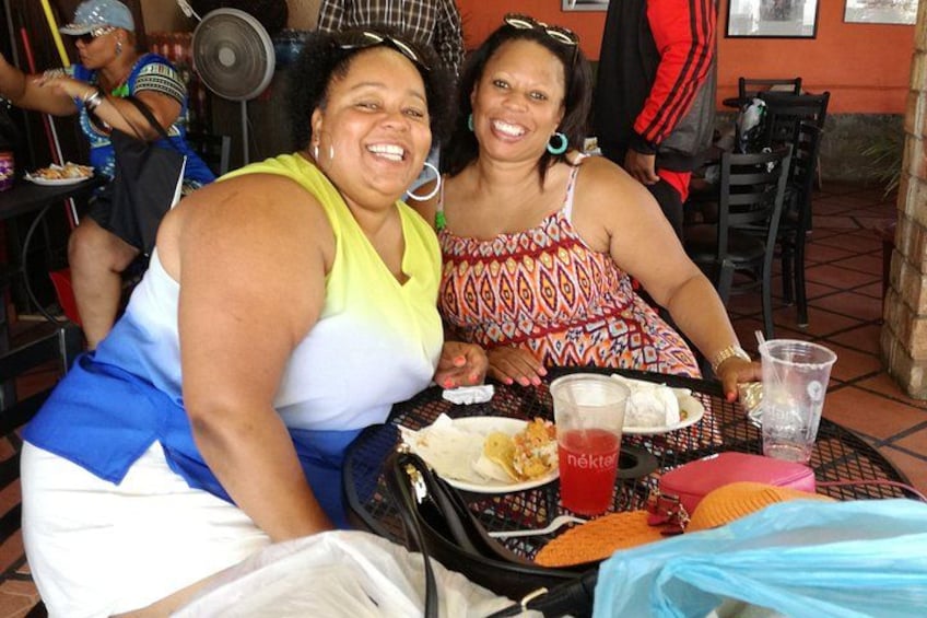 Two women sitting at a table with food and drinks. 3