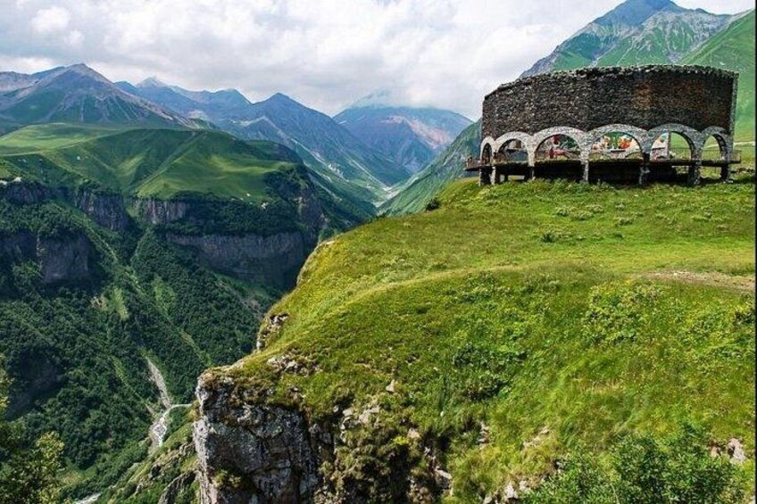 A stone structure with arches on a hillside overlooking a valley. 4