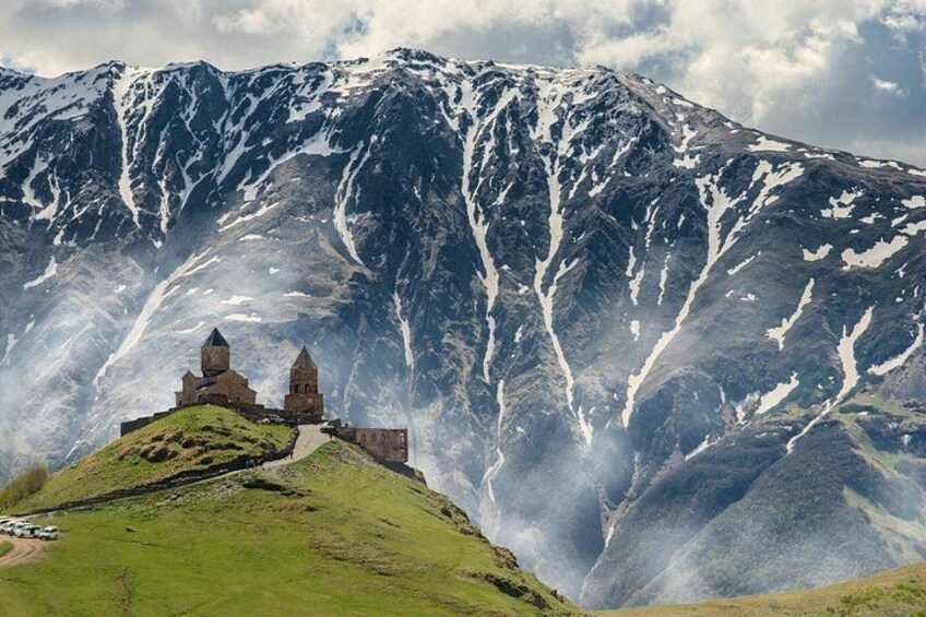 A historic church on a green hill with a snow-capped mountain in the background. 2