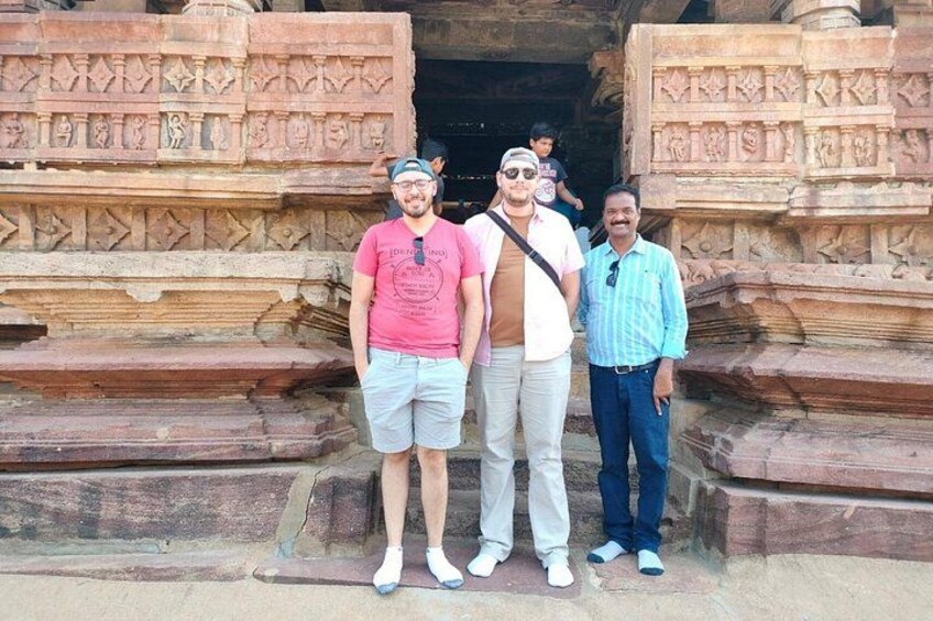 Three people standing in front of an ancient stone structure with intricate carvings. 4