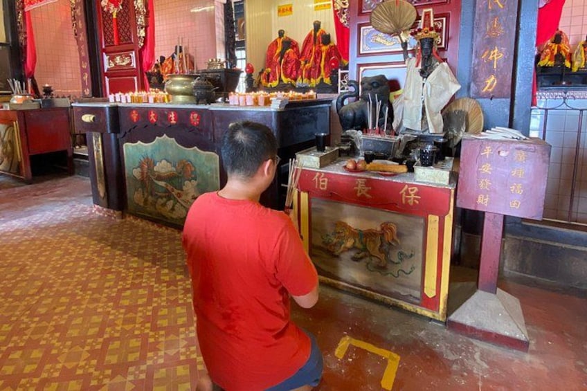 A man praying at a temple altar with religious statues and offerings. 4