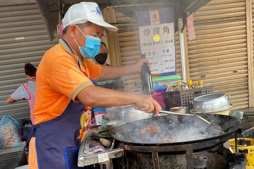 A street food vendor cooking at a stall with a signboard in the background. 1