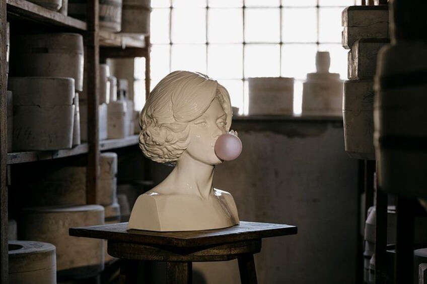 A bust sculpture on a table in a room with shelves of pottery. 1