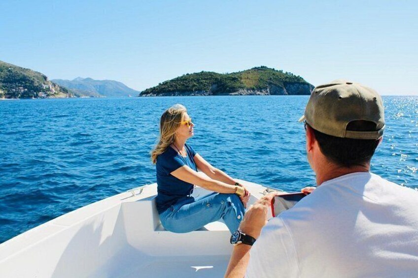 Un bateau sur une mer calme, avec une femme et un homme à bord, un ciel dégagé et une île verdoyante à l’horizon. 5