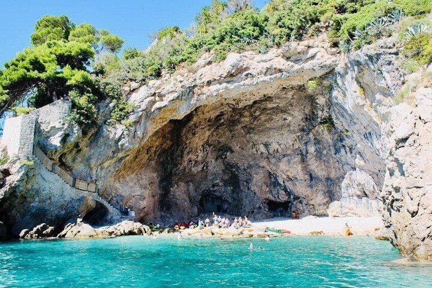 Une falaise rocheuse avec une entrée de grotte, une mer turquoise et des gens qui se baignent. 3
