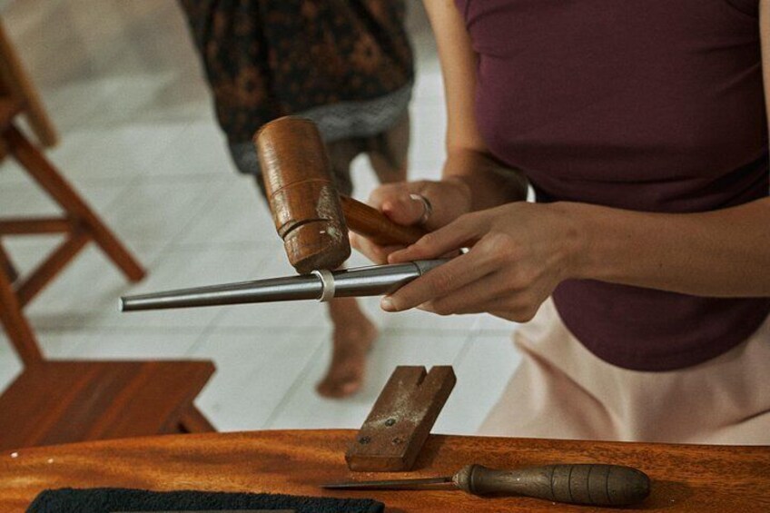 A person using a hammer and a metal rod, possibly for crafting or construction. 2