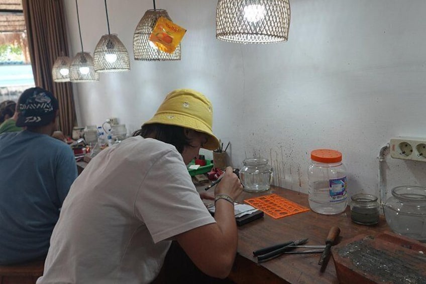 A person wearing a yellow hat working at a wooden table with various tools and containers. 3