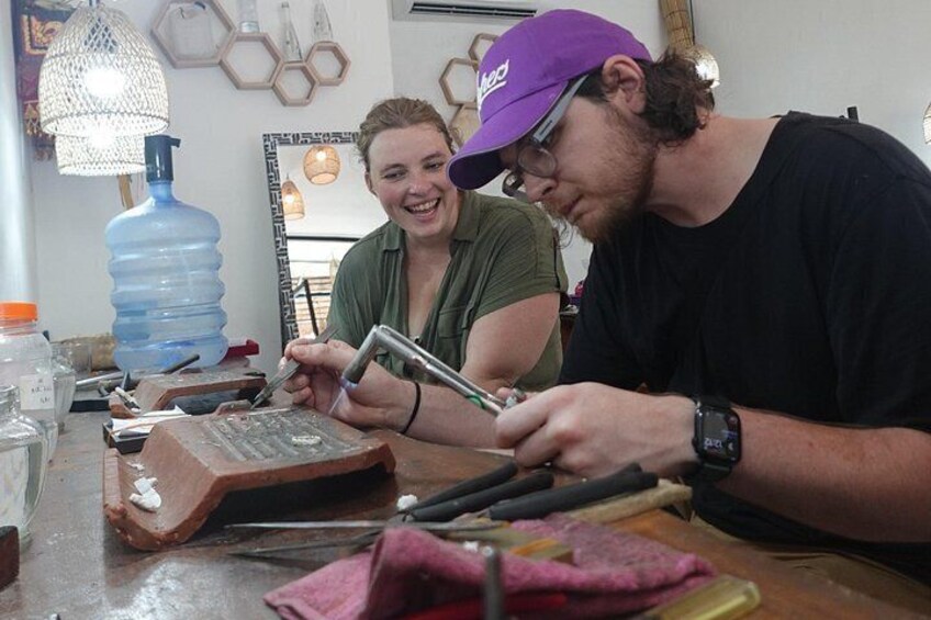 Two people working on a craft project with tools and a water bottle on a table. 4