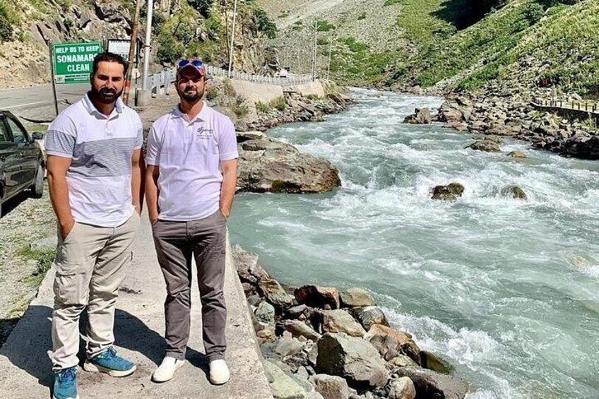 Two men standing by a river with a sign that reads 'HELP IS TO KEEP SONAMAR CLEAN.' 3
