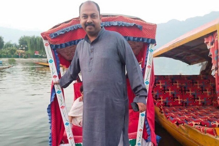 A man standing next to a traditional boat with a red and blue patterned canopy. 2