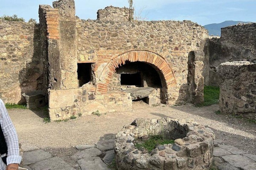 An ancient stone structure with a large arched oven and a stone well. 1