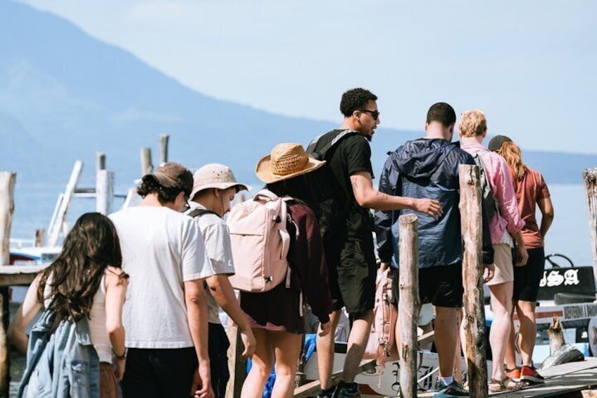 A group of people standing on a dock by a body of water with mountains in the background. 4