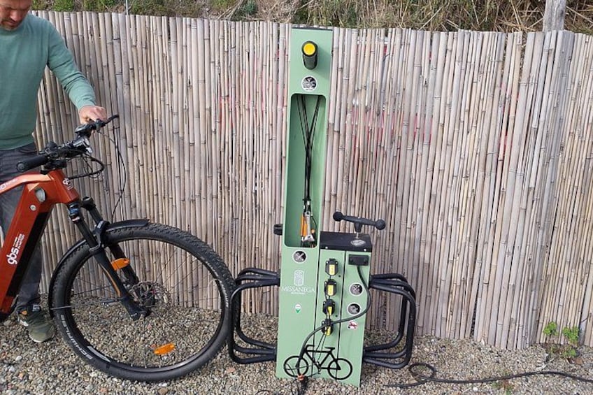 A bicycle, a green electric bike charging station, and a wooden fence. 2