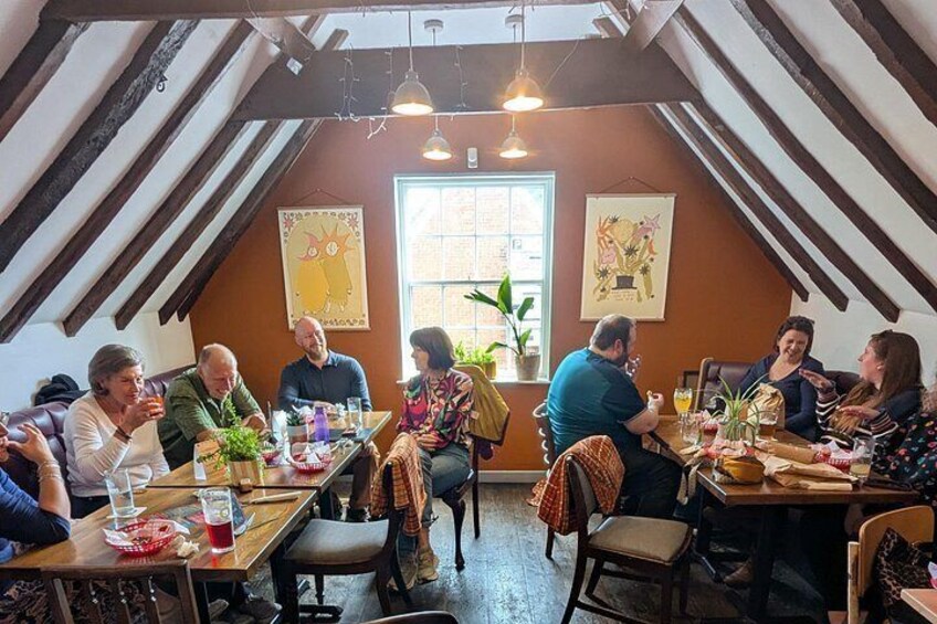 A group of people sitting at a wooden table in a room with sloped ceilings and wooden beams. 2