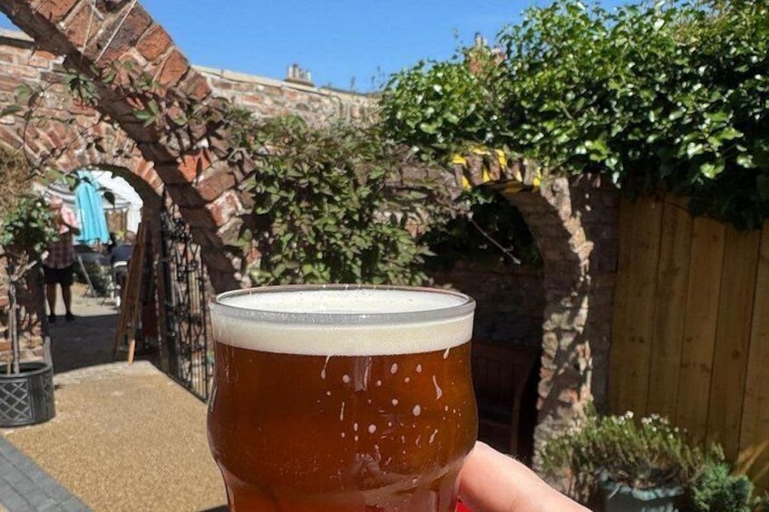 A glass of beer held in front of a brick archway with greenery. 5