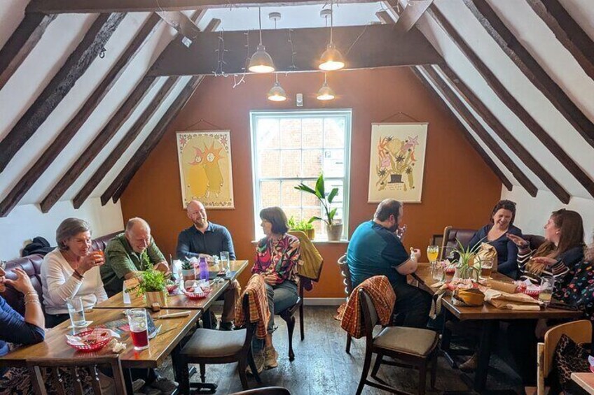 A group of people seated around a table in a room with wooden beams and a window. 4