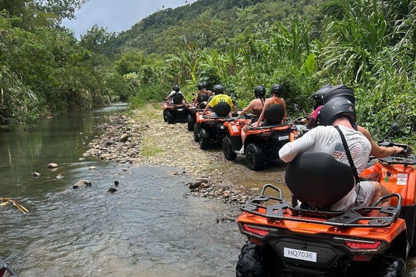 A group of people on ATVs along a riverbank surrounded by greenery. 4