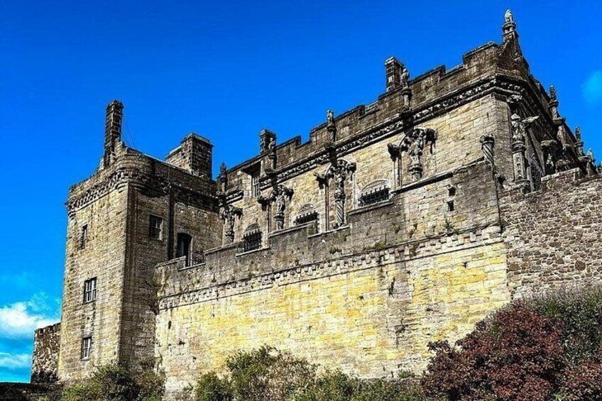 Un castillo de piedra histórico con almenas, un cielo azul despejado y un jardín bien cuidado. 3
