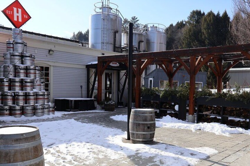 A brewery with large metal tanks, wooden barrels, and a snowy ground. 3