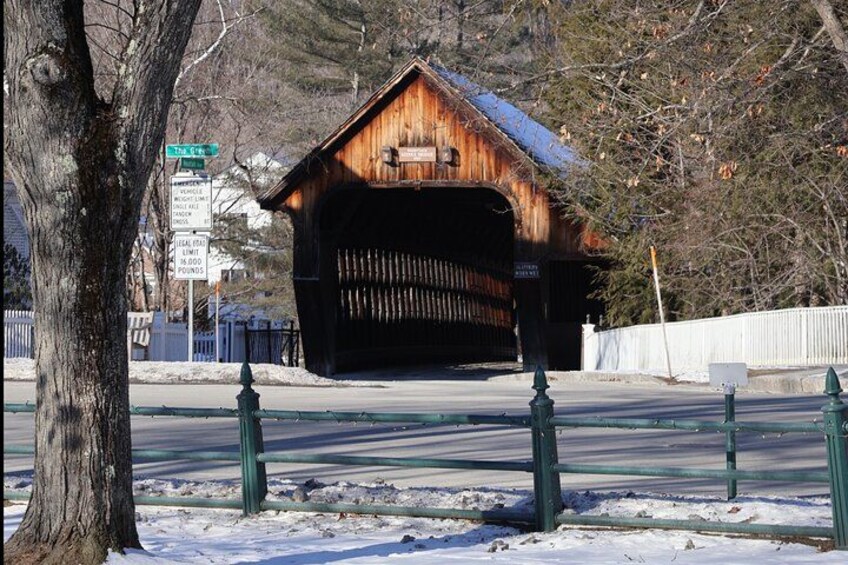 A covered bridge, snow on the ground, and a street sign in the background. 4