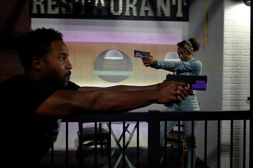 Una persona sosteniendo una pistola, otra persona apuntando con una pistola, y un letrero de restaurante al fondo. 3