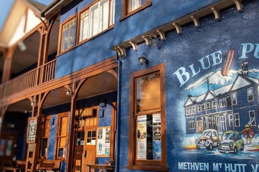 A building with a mural of a house and cars, and the text 'BLUE PUB' and 'METHVEN M HUTTE V'. 5