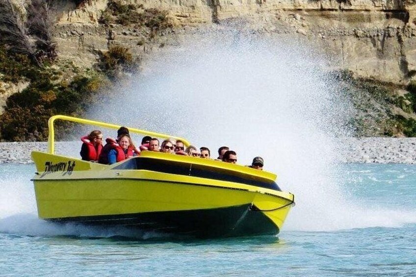 A yellow boat with passengers, moving through water with a cliff in the background. 3