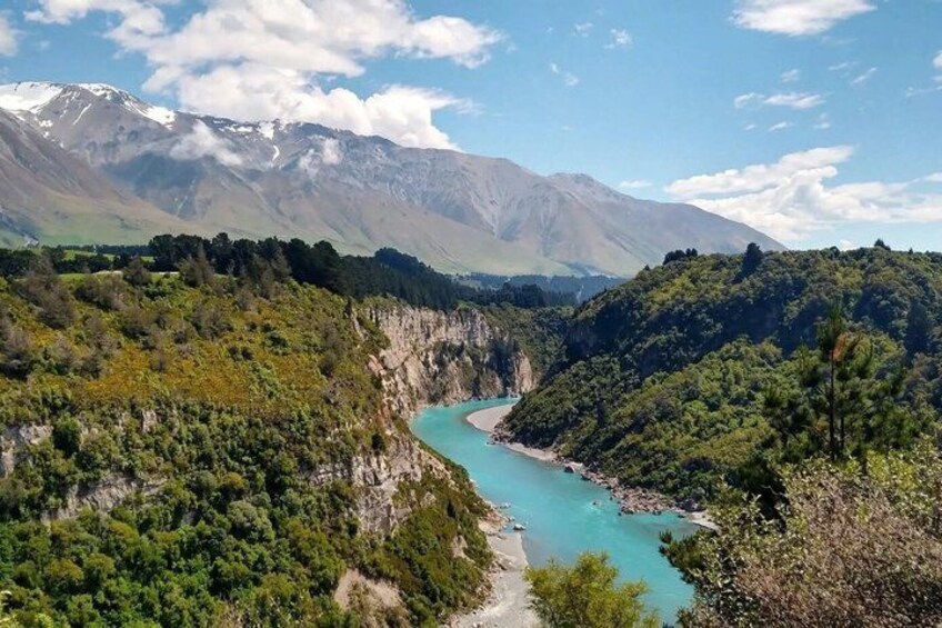 A turquoise river winding through a valley with dense greenery and mountains in the background. 5