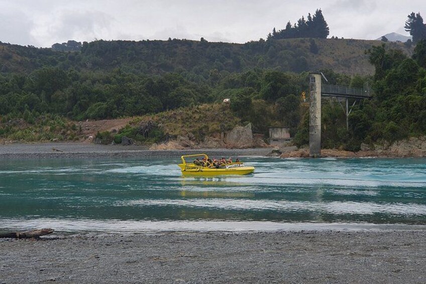 A yellow boat on a river with a bridge and forested hills in the background. 2