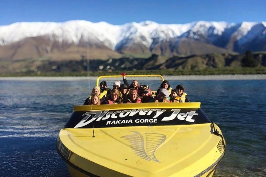 A yellow boat named 'Discovery Jet' with passengers, on a lake with mountains in the background. 3