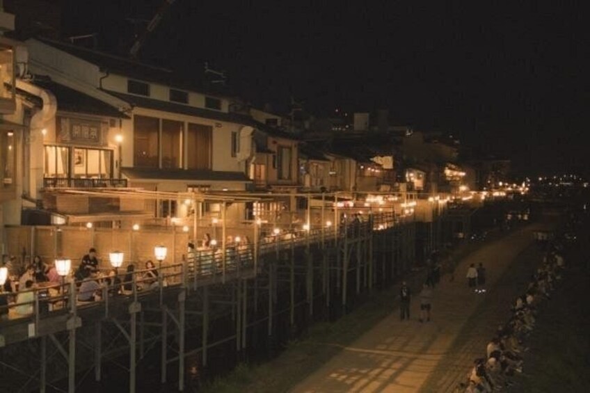 A nighttime coastal street with buildings, a pedestrian walkway, and people. 3