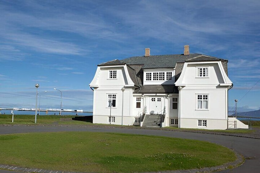 A white house with a grey roof, a staircase, and a grassy area in front. 5