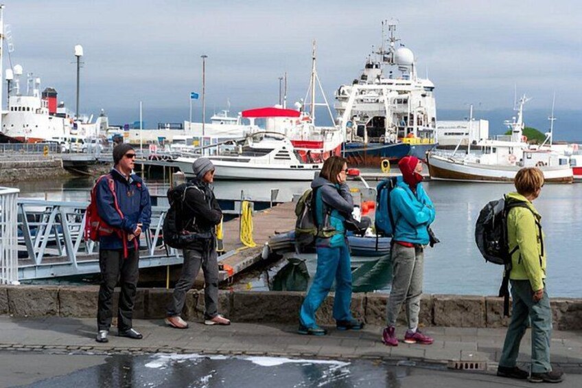Eine Gruppe von Menschen steht am Ufer, im Hintergrund sind Boote und ein großes Schiff zu sehen. 4