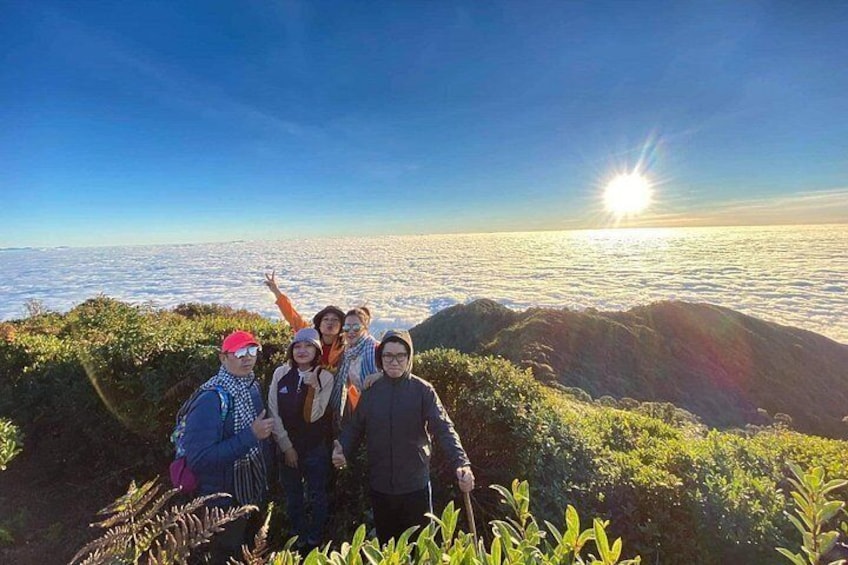 A group of people on a mountain with a view of the ocean and the sun setting in the background. 1