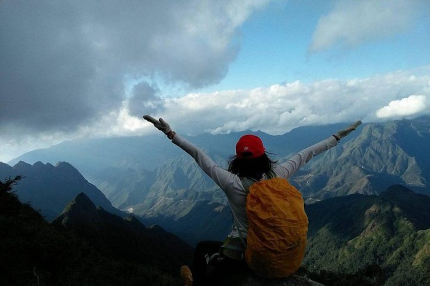 A person sitting on a mountain with arms outstretched, facing a mountain range. 2