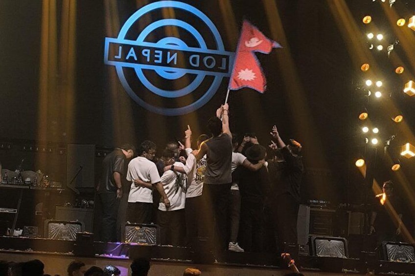 Een groep mensen op een podium, met een groot logo en een vlag. 3