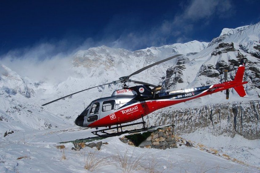 Un hélicoptère rouge et noir, orné des logos « TOROED » et « SIMRIX », est garé sur une montagne enneigée. 1