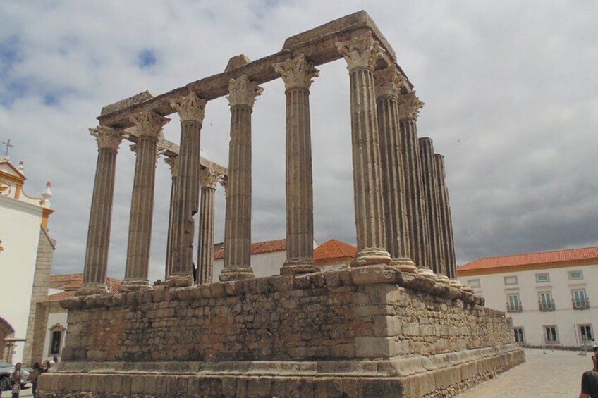Columnas antiguas de una estructura histórica, una base de piedra y un edificio con techo rojo al fondo. 2