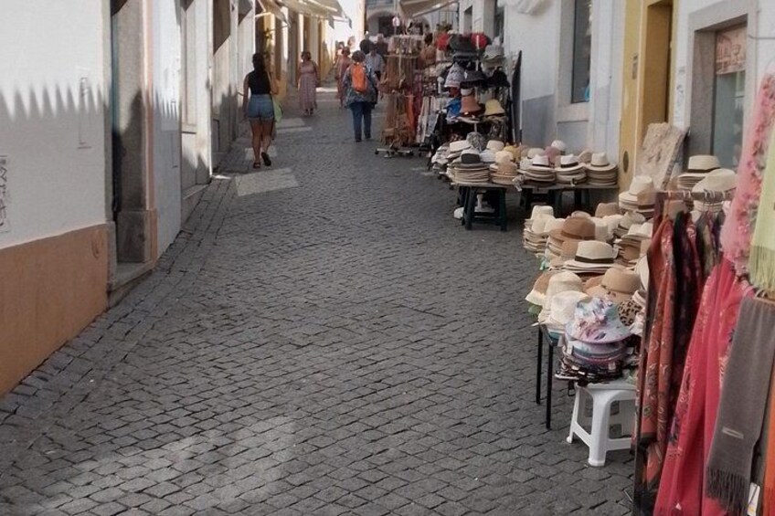Una calle adoquinada con tiendas a ambos lados, incluyendo un puesto que vende sombreros. 5