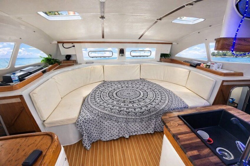 Bootinterieur met een rond zithoek, een centrale tafel en een raam met uitzicht op de zee. 2