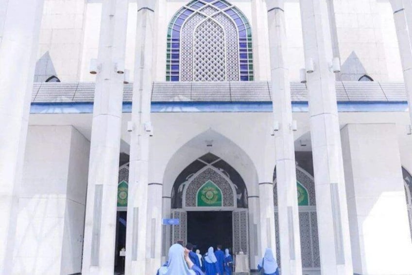 Un grand bâtiment blanc doté d’une entrée centrale en arc de cercle, d’une grande fenêtre ornée d’un motif géométrique et d’un décor vert et blanc au sommet de l’arc. 2