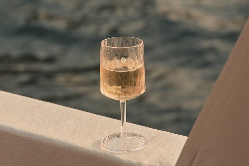 Ein Glas Weißwein auf einem Balkon, im Hintergrund ein Gewässer. 5