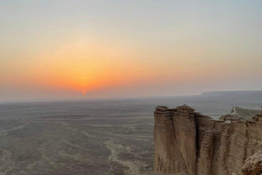 A desert landscape with a sunset, rocky cliffs, and a vast open plain. 4