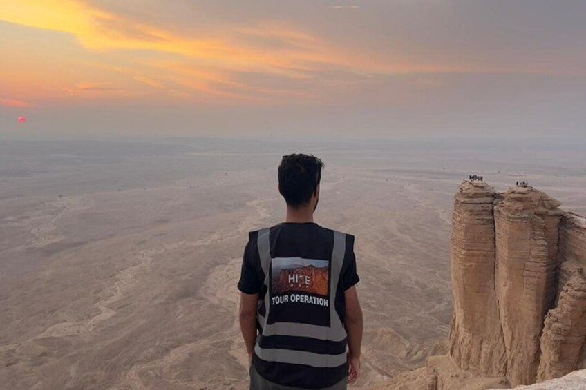 A person standing on a cliff overlooking a vast desert landscape with a sunset in the background. 3