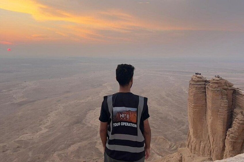 A person standing on a cliff overlooking a vast desert landscape during sunset. 3