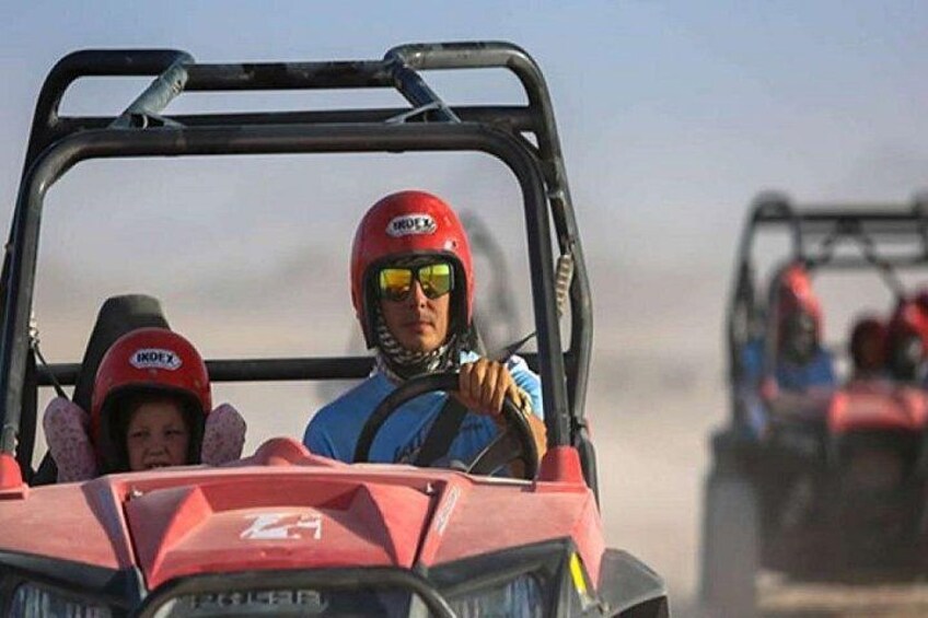 A person in a red ATV with a helmet and a child in a pink helmet. 1