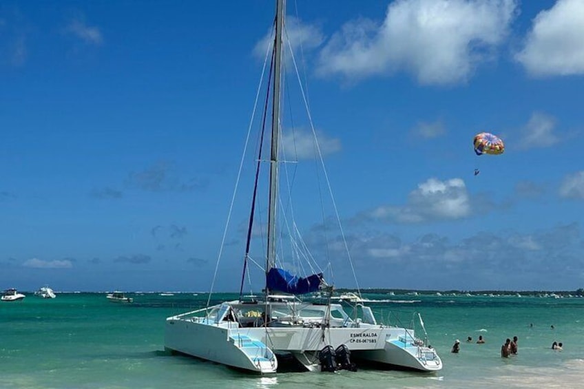 Un velero atracado en una playa con agua turquesa cristalina y algunas personas a lo lejos. 3